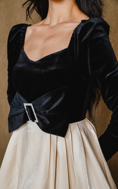 Long sleeve, black dress has ribbon belt and beige, satin bow swing skirt.