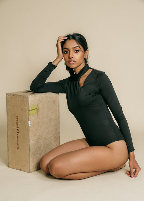 Black, fitted, long sleeve bodysuit has cutaway detail on front.